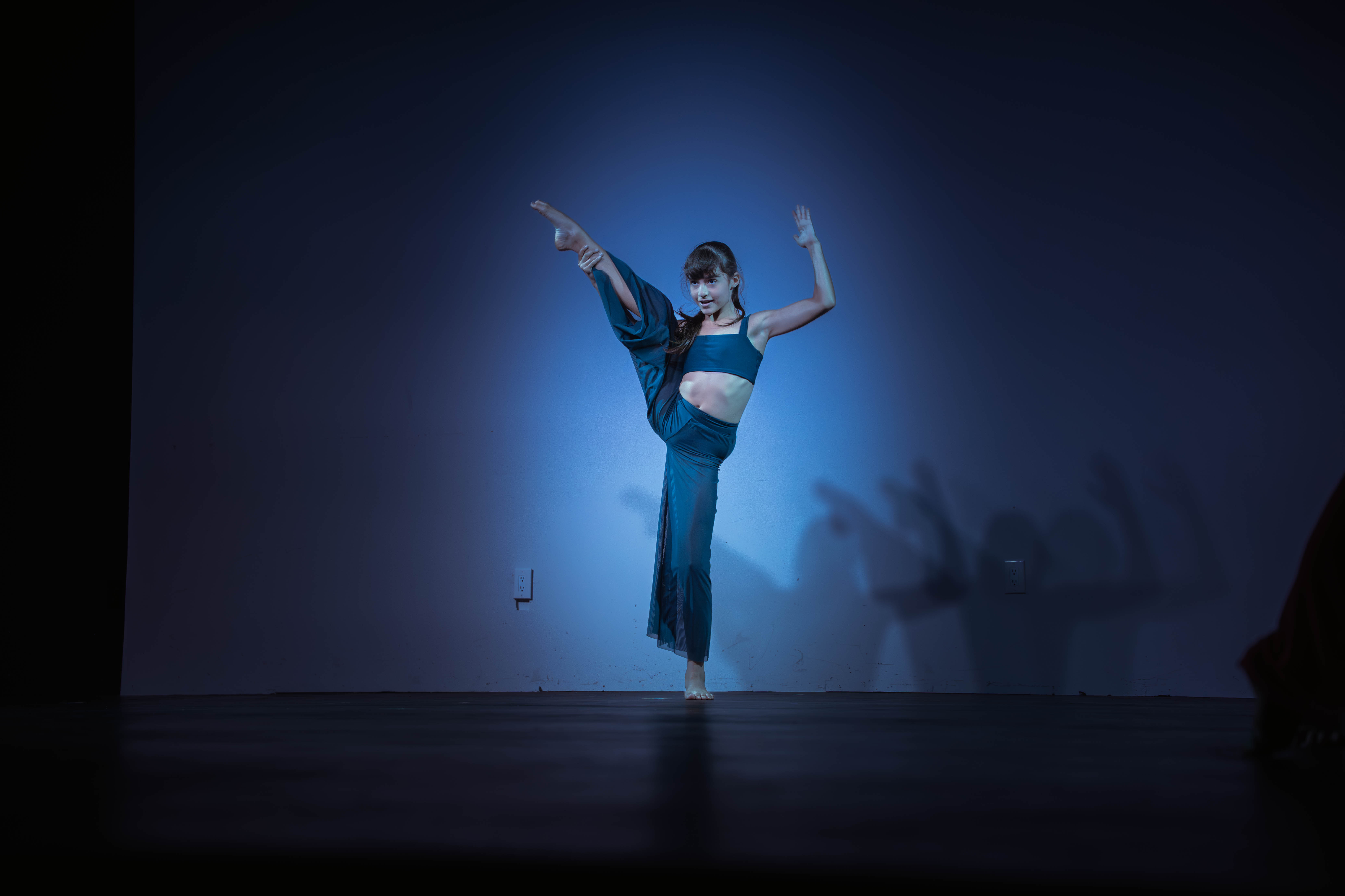 VelaDance dancer in a high leg extension against blue stage light — professional contemporary dance company South Jersey